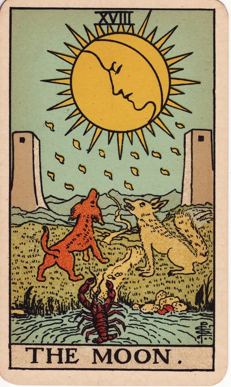 Carta de La Luna — luna con rostro sobre un sendero con lobo, perro y cangrejo emergiendo del agua, baraja Rider-Waite-Smith